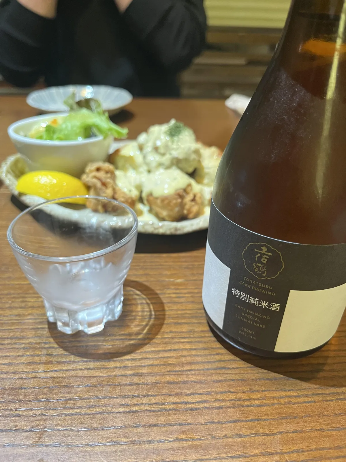 テーブルに置かれた土佐鶴 特別純米酒の300mlボトルと、タルタルソースがかかった揚げ物料理