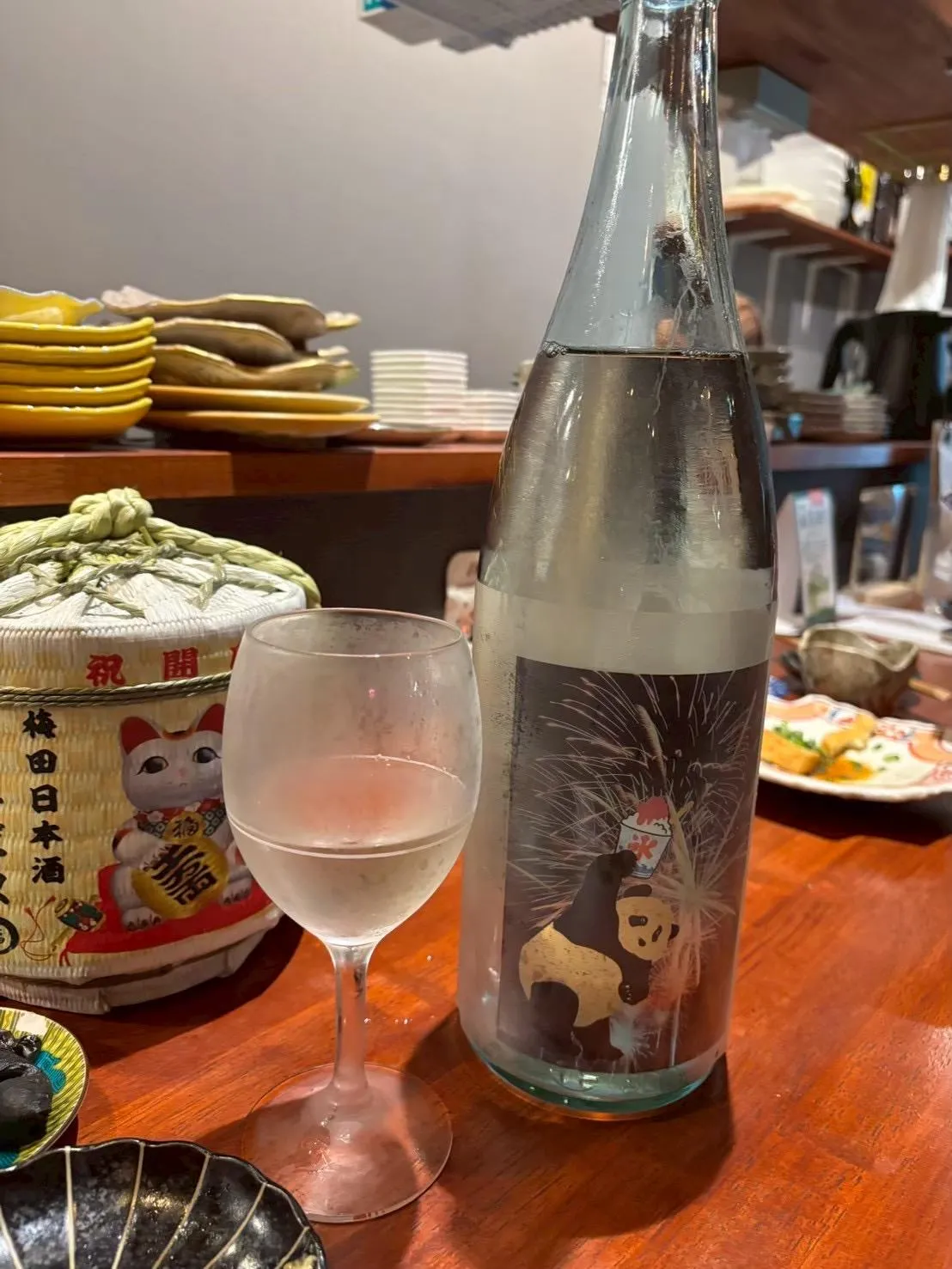 カウンターに置かれた純米爽酒 Summer Panda☆のボトルと冷えたグラス、奥には招き猫の小さな樽