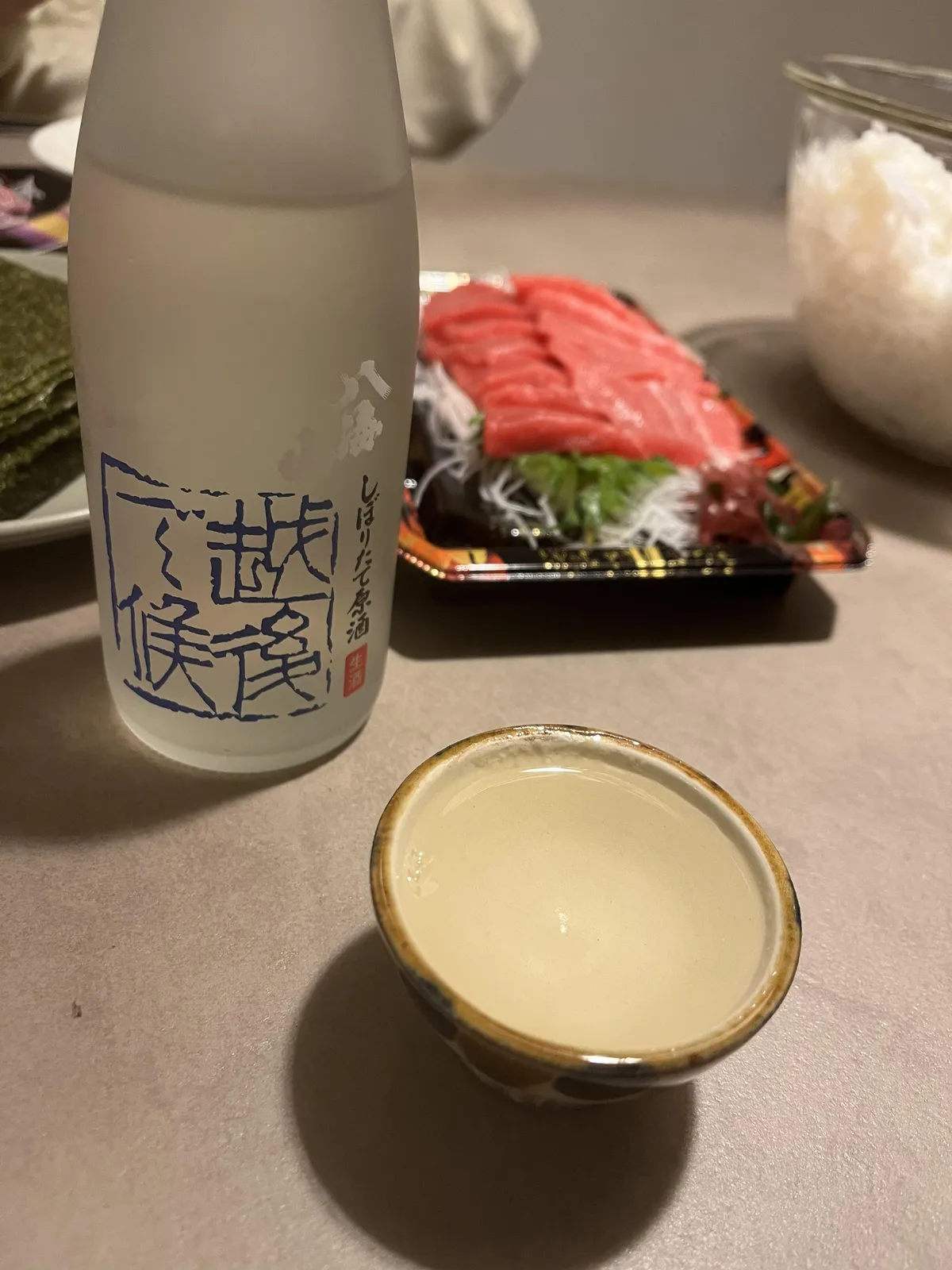 八海山しぼりたて原酒 越後で候のボトルと、酒器に注がれたお酒、マグロのお刺身などの食卓風景