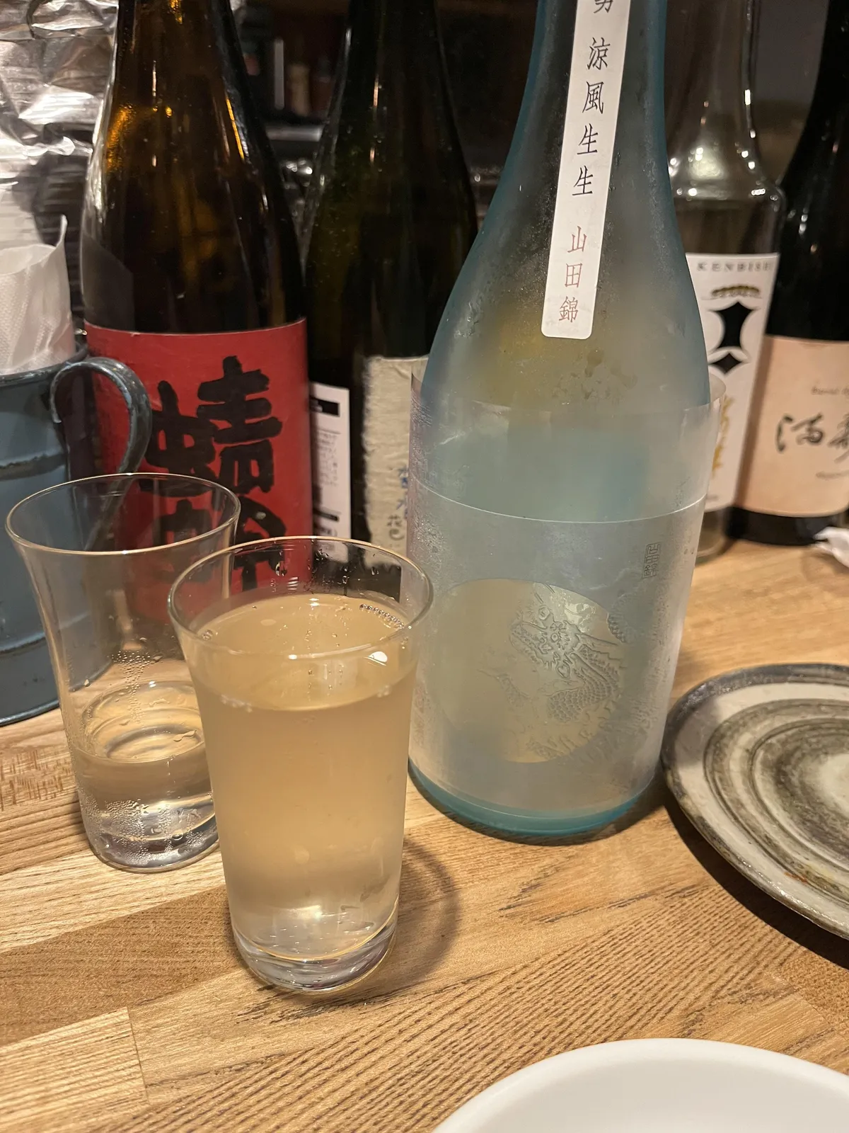 青いフロスト瓶の龍勢 涼風生生と、手前のグラスに注がれたお酒