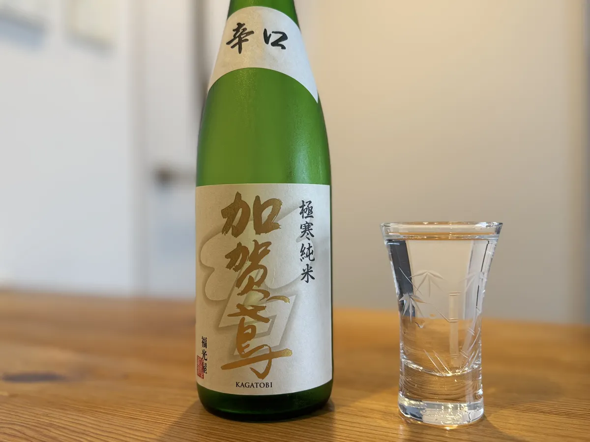 木目調のテーブルに置かれた加賀鳶 極寒純米 辛口のボトルと、お酒が注がれた竹の模様入りのグラス