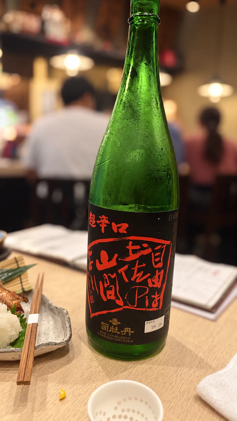 結露した緑色の瓶に、黒地に赤い文字で銘柄が書かれたラベルが貼られた日本酒のボトル