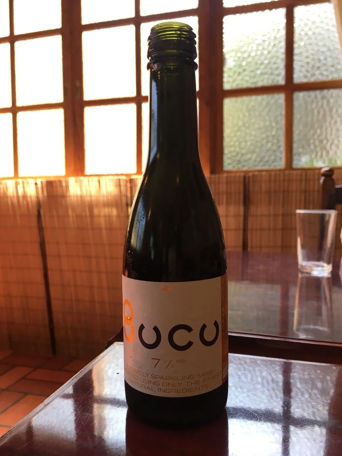 逆光の窓際に置かれたスパークリング純米酒 Bucuのボトル