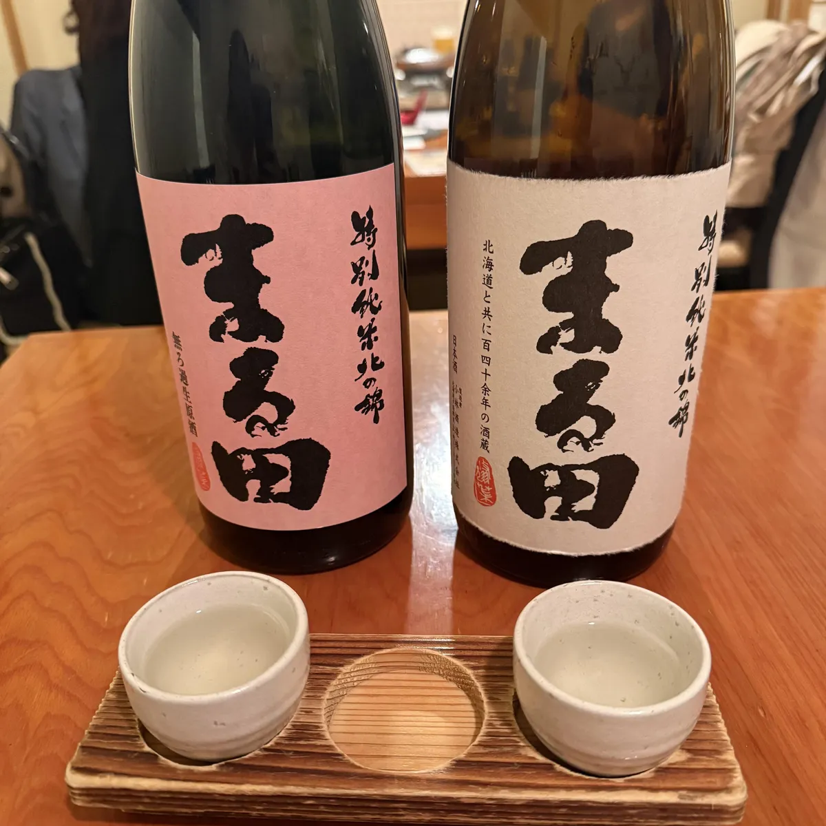 木目のテーブルに並ぶ2種類の「特別純米酒 まる田」と、お猪口に注がれた日本酒