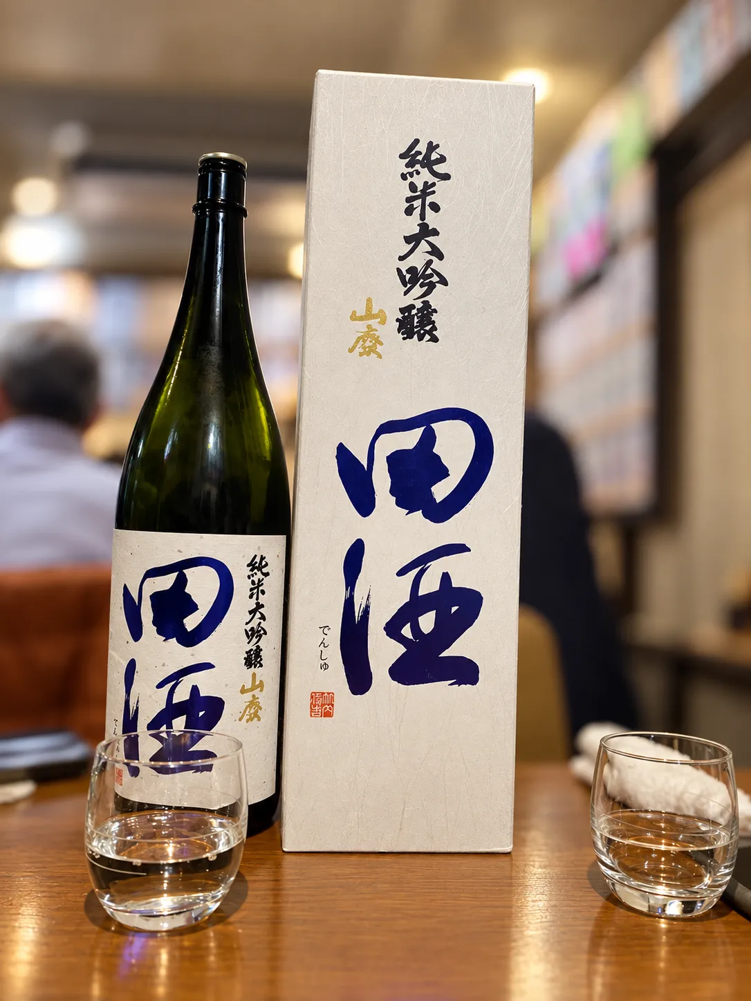 テーブルに置かれた田酒 純米大吟醸 山廃のボトルと専用の箱、注がれたグラス