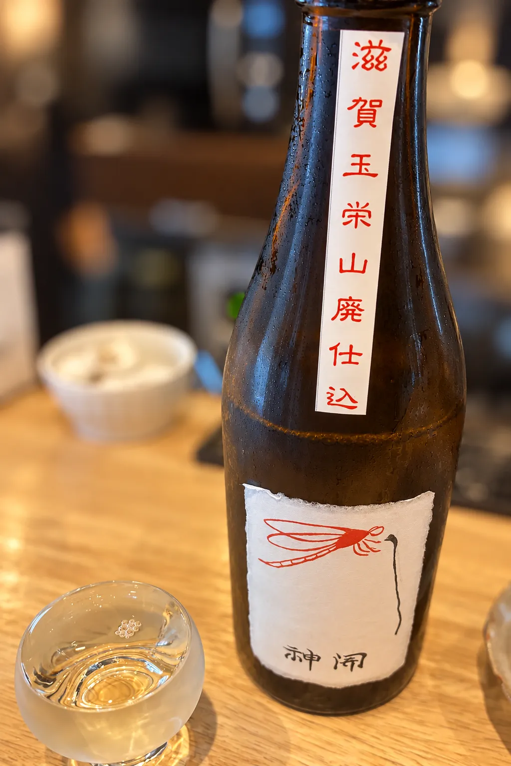 赤とんぼが描かれた神開のボトルと、グラスに注がれた日本酒
